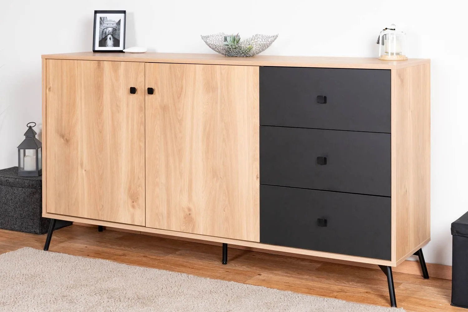 Kommode Lincolnia 04, Farbe: Eiche / Schwarz - Abmessungen: 85 x 160 x 40 cm (H x B x T), mit 2 Türen, 3 Schubladen und 4 Fächern